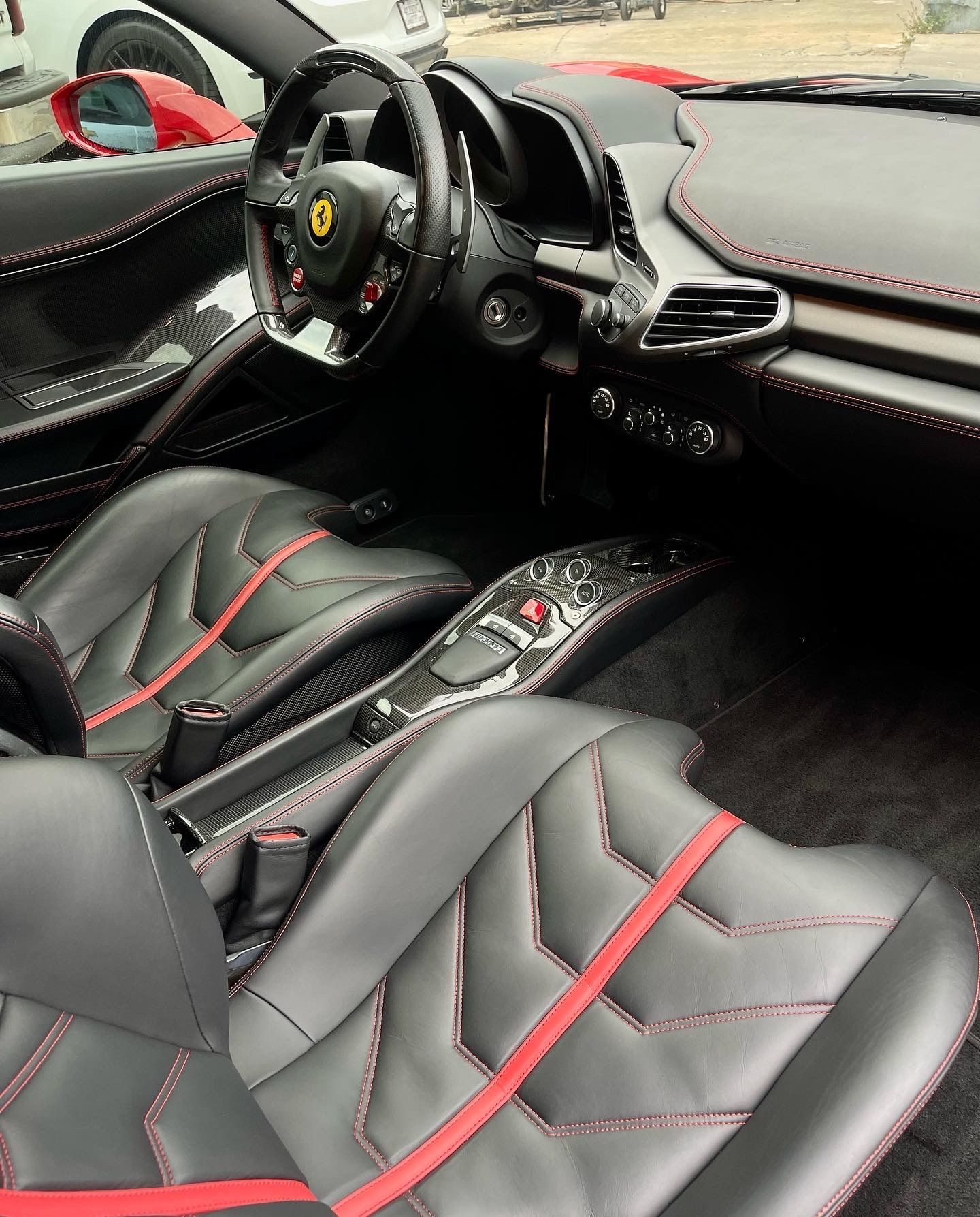 Black leather Ferrari interior with red stitching. Steering wheel, seats, and console visible.