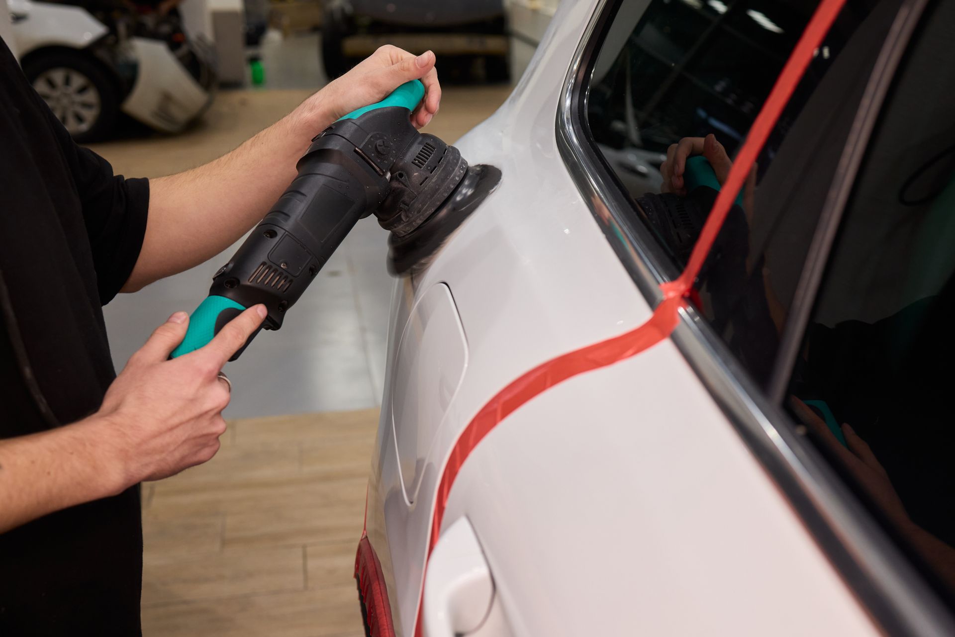 Gloved hand applying a ceramic coating to a black car surface, reflecting light.