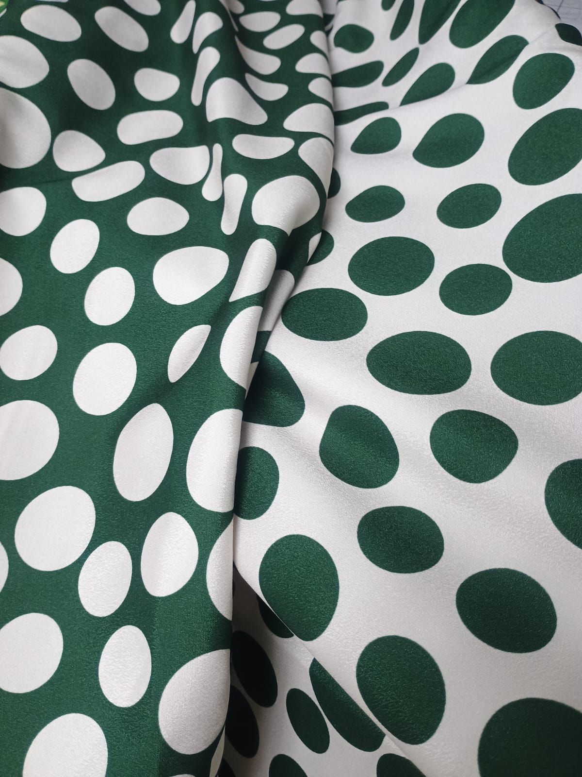 Vista de cerca de una tela que presenta un patrón repetido de manchas irregulares y redondeadas de color verde oscuro