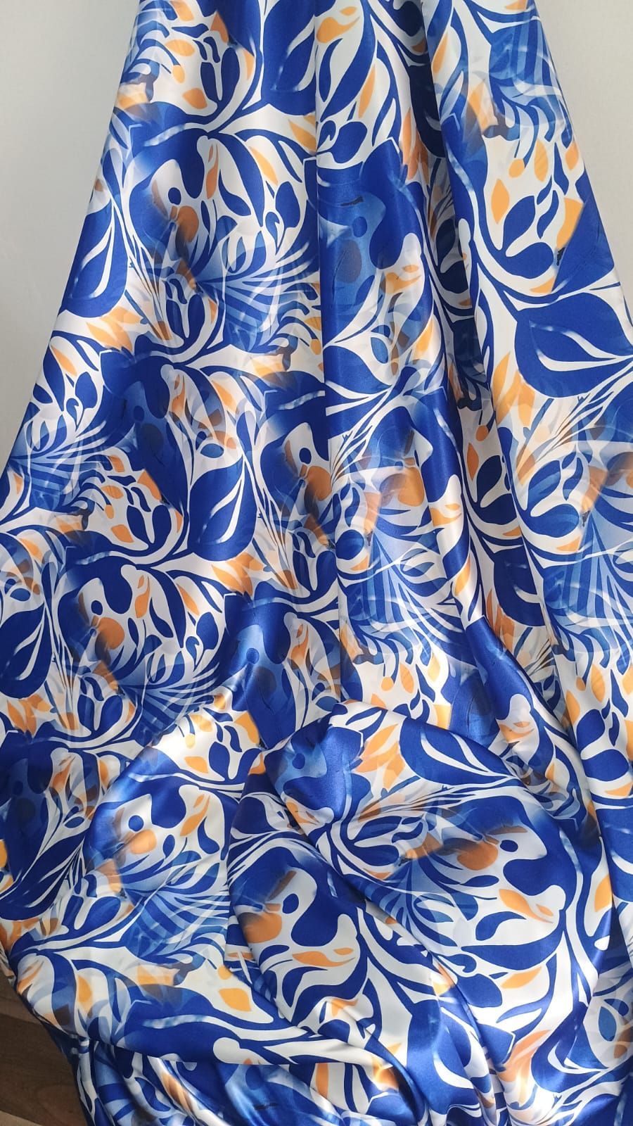 Una tela suave y drapeada que presenta un intrincado patrón floral en tonos azul real, blanco y naranja suave.