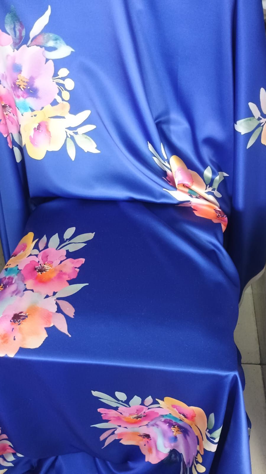 Una tela azul real vibrante que presenta un estampado floral estilo acuarela con flores rosas, durazno y amarillas.