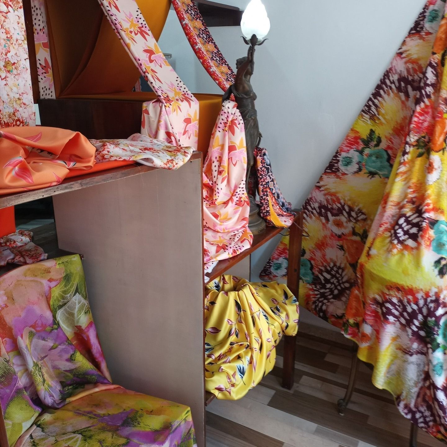 Telas florales con estampados brillantes cubren muebles y una lámpara en una habitación con piso de baldosas.