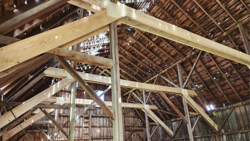 The interior of a barn showing unfinished wooden timber framing and a partially collapsed, weather-worn roof.