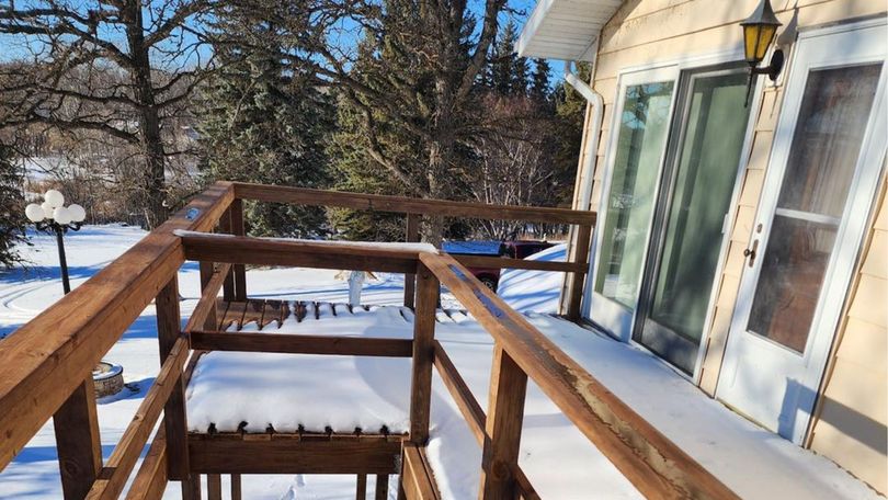 A snow-covered wooden deck with railings extends from the sliding glass doors of a house on a sunny, winter day.