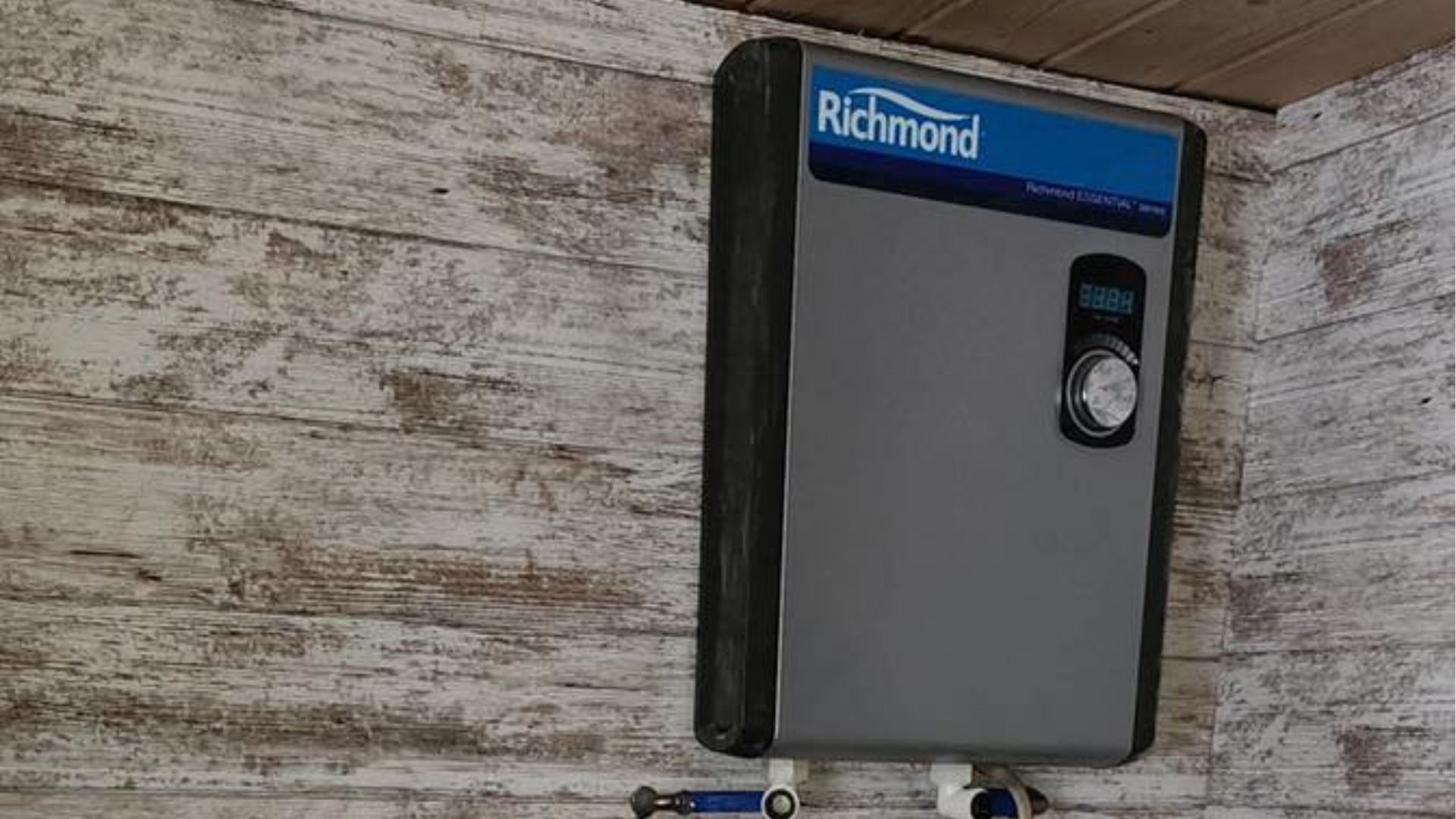 A gray Richmond electric tankless water heater mounted on a white wood-paneled wall.