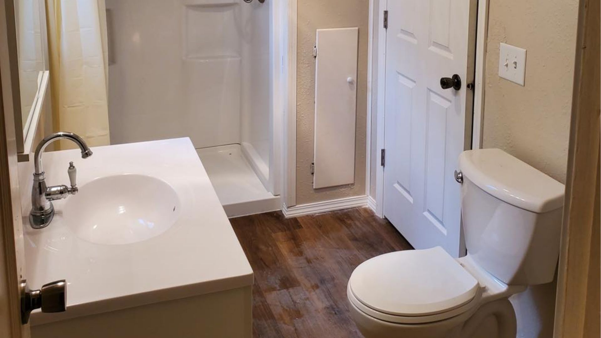 A small bathroom with a white vanity sink, a toilet, a walk-in shower, and wood-look flooring.