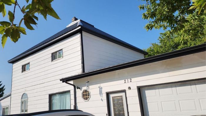 A white, two-story house with a black roof and garage, featuring a small circular sign near the front door.