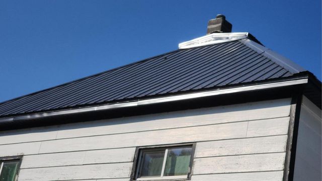 White house with black trim and a dark, corrugated metal roof under a clear blue sky.