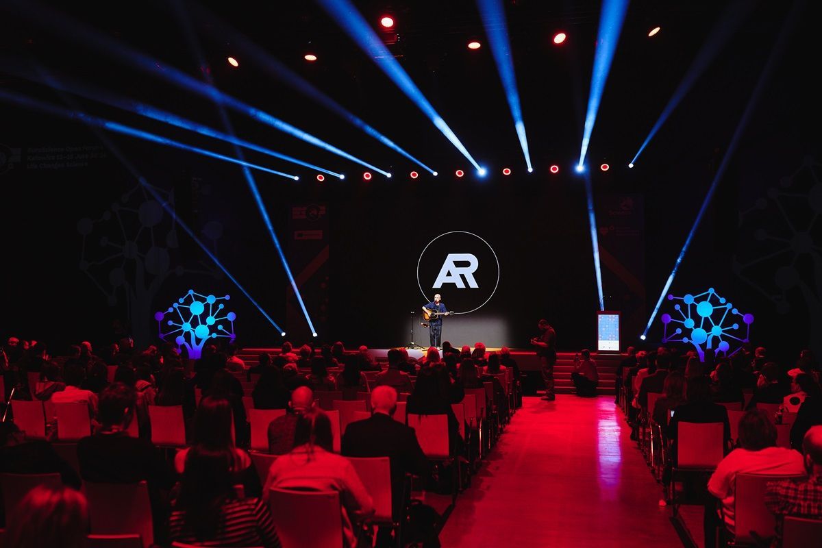 A group of people are sitting in front of a stage with a logo that says ar on it.