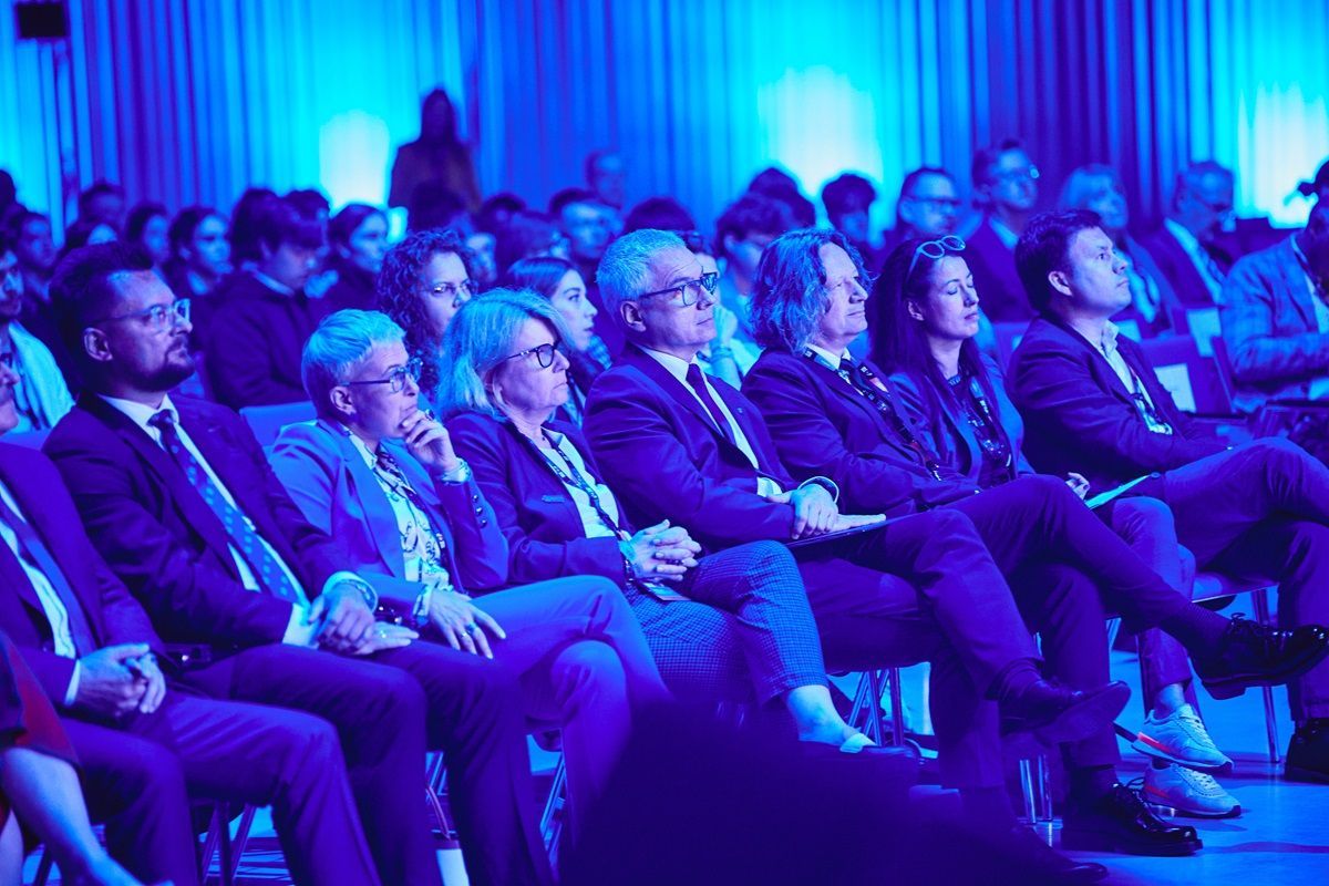 A large group of people are sitting in a room with blue lights.