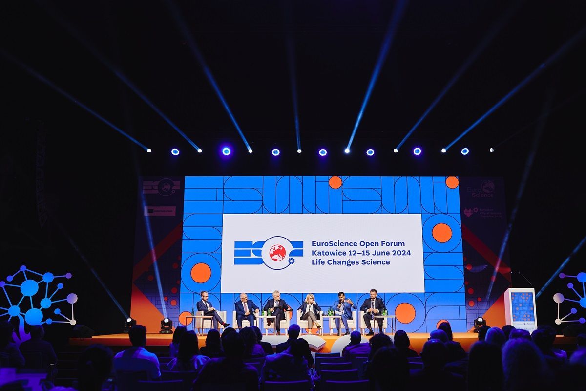 A group of people are sitting in front of a large screen at a conference.