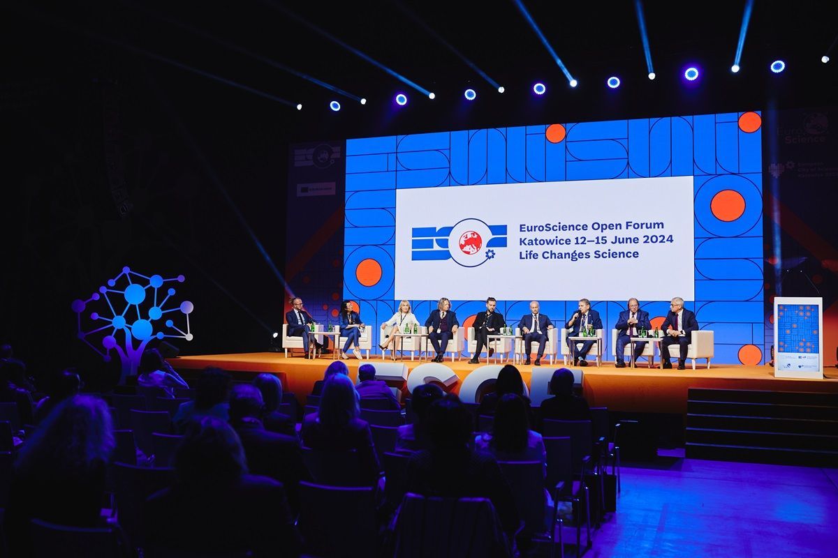 A group of people are sitting in front of a large screen on a stage.