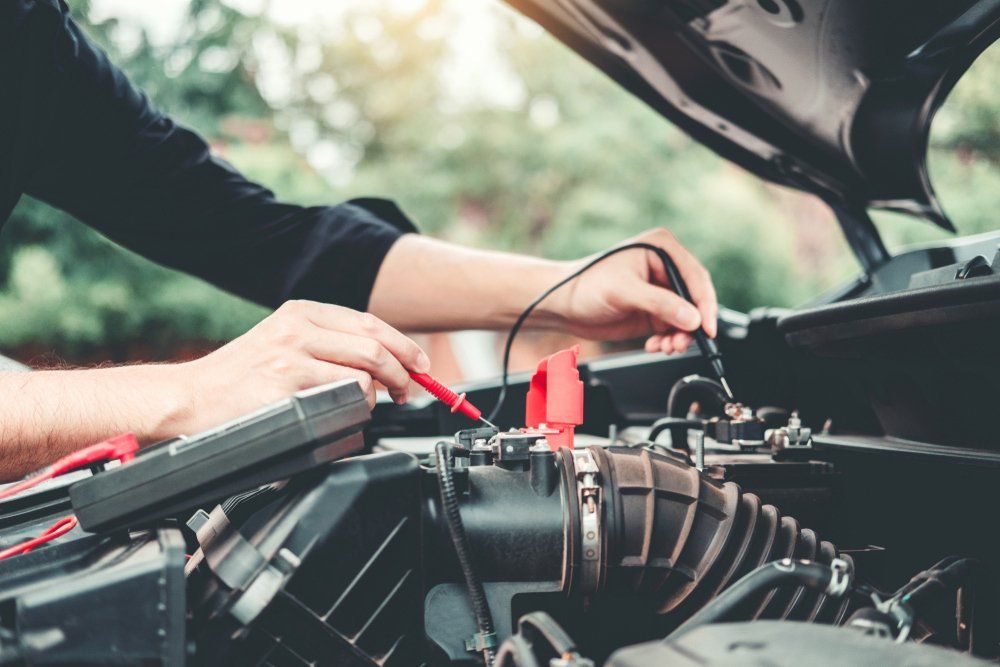 An auto electrician testing a car battery with a multimeter under the bonnet