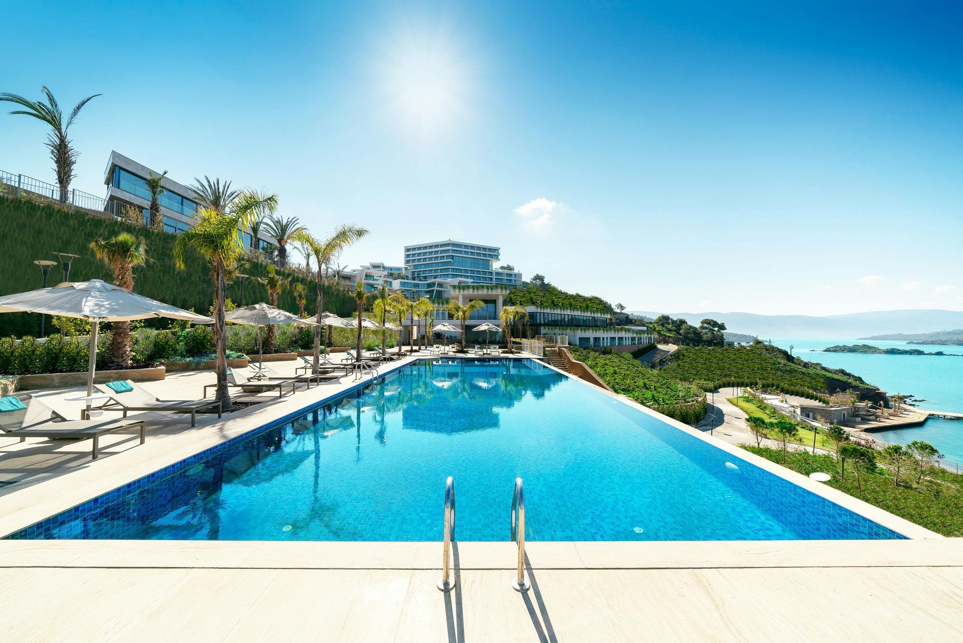 Infinity pool overlooking turquoise water, resort buildings, and sunny sky.