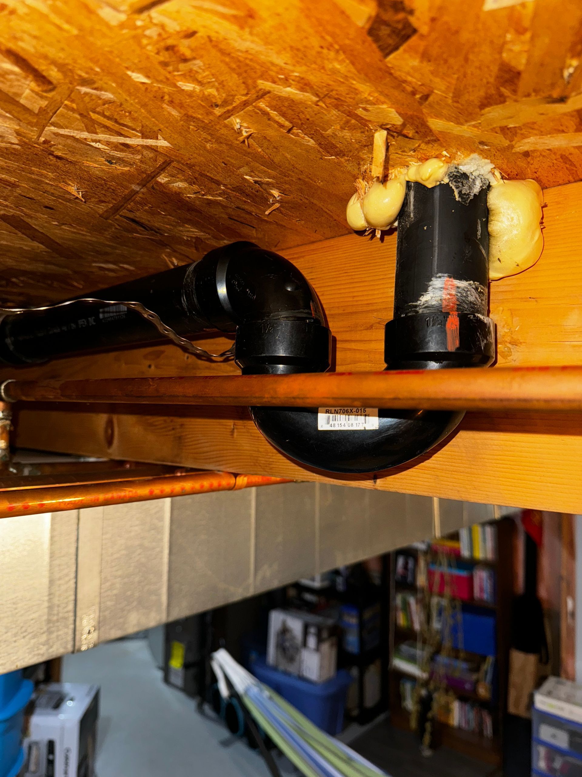 Black plumbing pipes and fittings attached to wooden joist; spray foam present.
