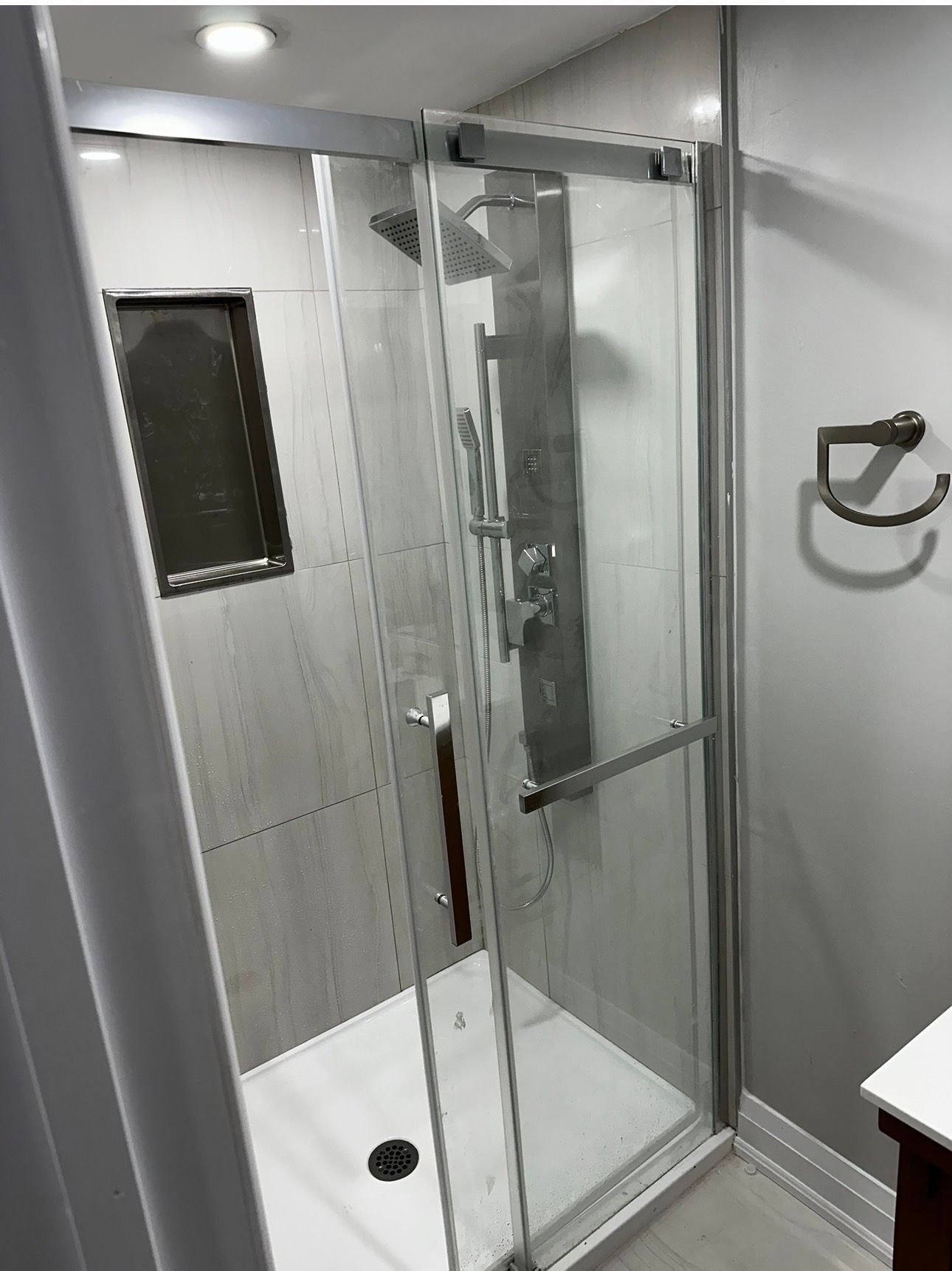 A modern shower with glass doors, a silver shower panel, and light-colored tile walls.