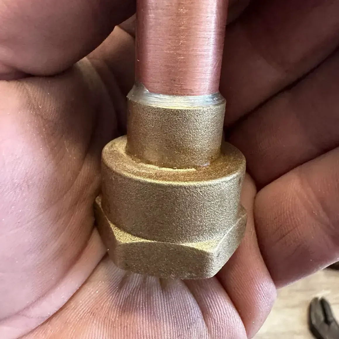 Close-up of a copper pipe connected to a brass fitting held in a person's hand.