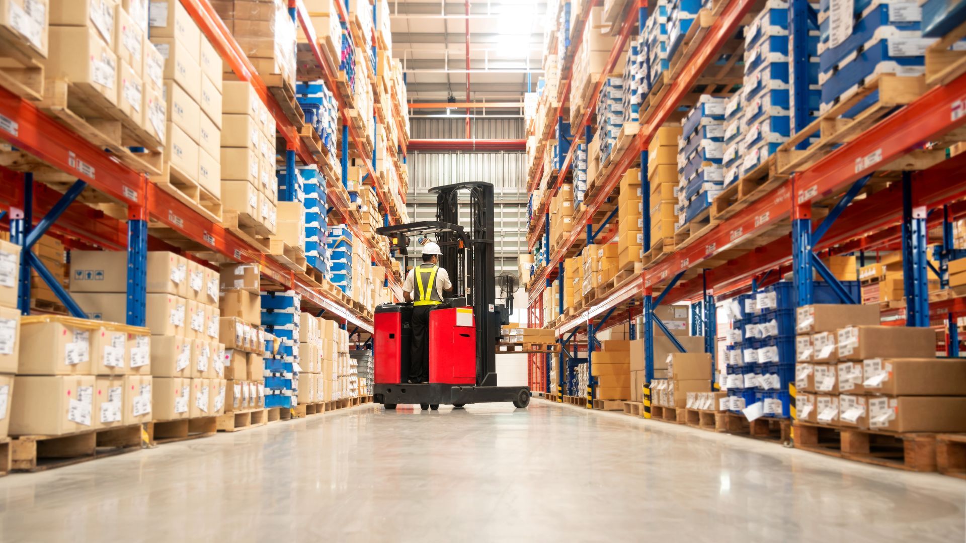 Warehouse aisle with a red forklift between tall shelves of boxed goods and pallets