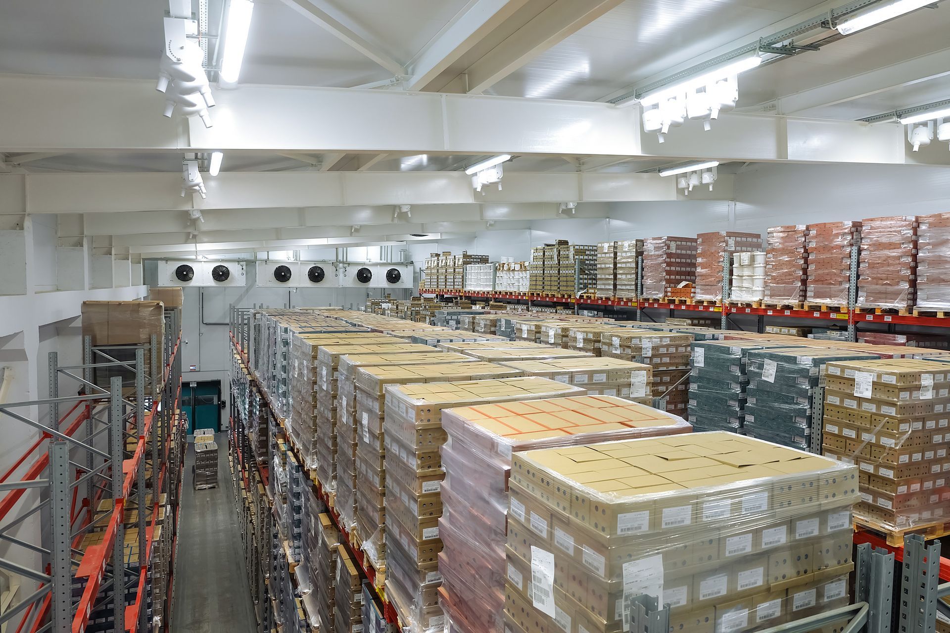 Large industrial cold storage room with rows of stacked palletized boxes on metal racks