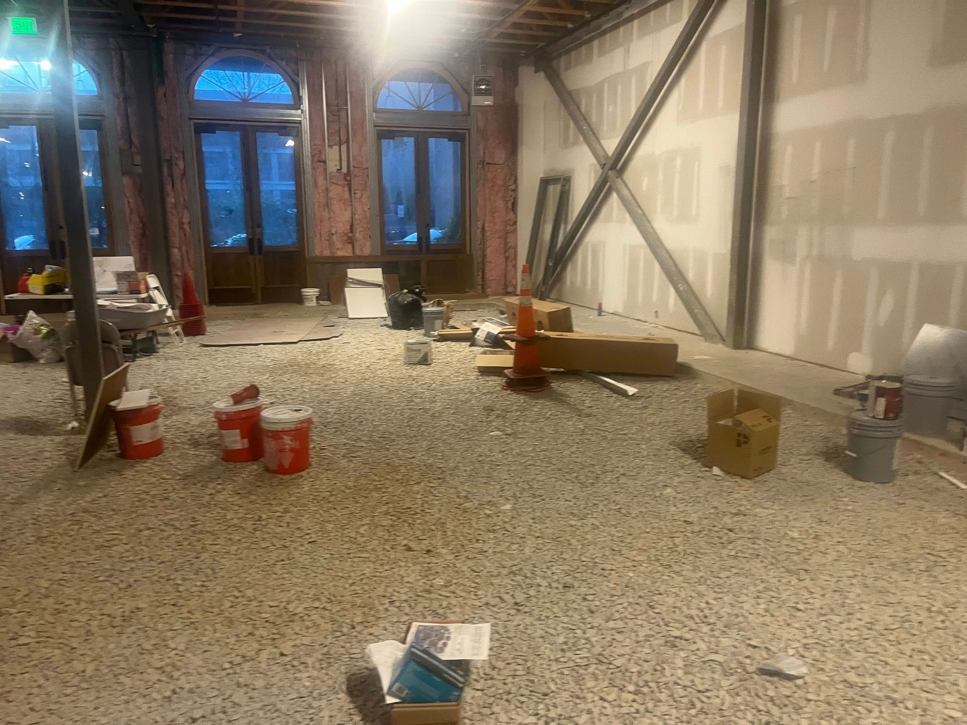 A construction site interior featuring a gravel floor, exposed wall studs, arched windows, and scattered work supplies.