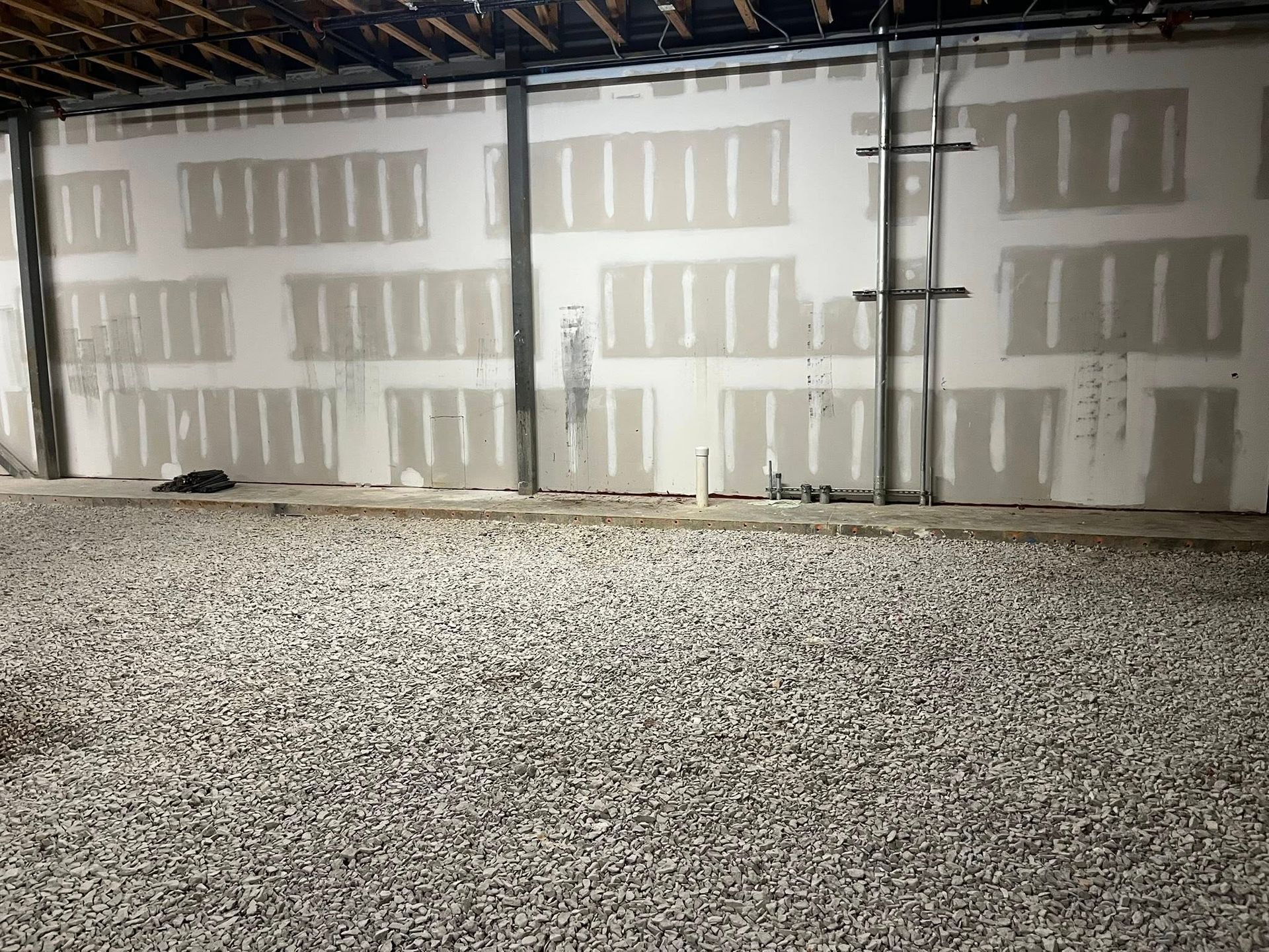 An unfinished room with a gravel floor and drywall panels installed on the walls between vertical metal support beams.
