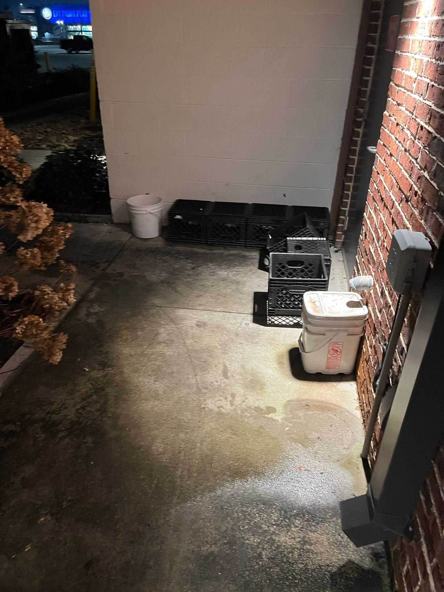A dimly lit brick walkway at night, featuring a stack of black crates and two white plastic buckets.