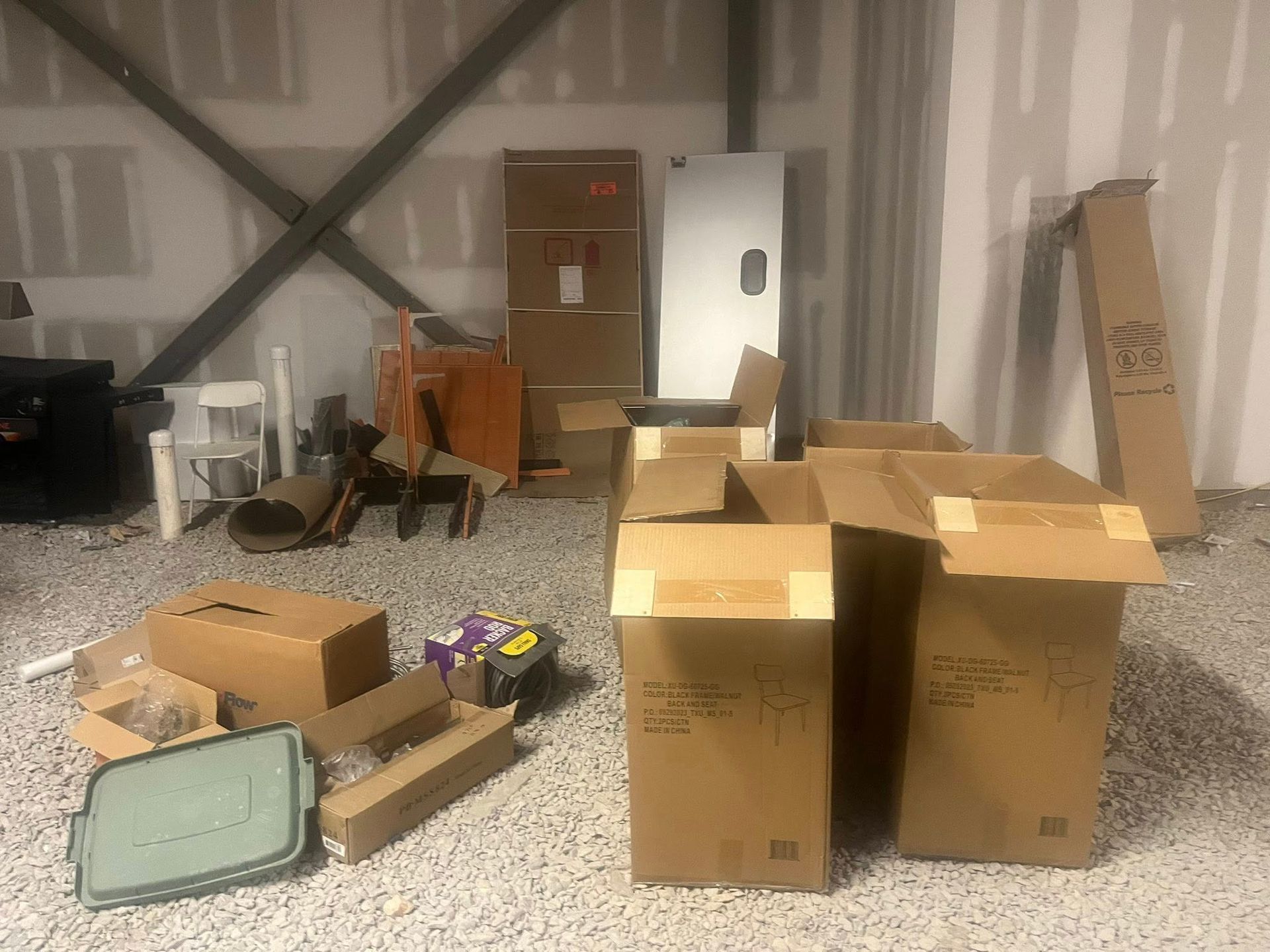 Cardboard boxes and miscellaneous packing supplies scattered on a gravel floor in a room under construction.
