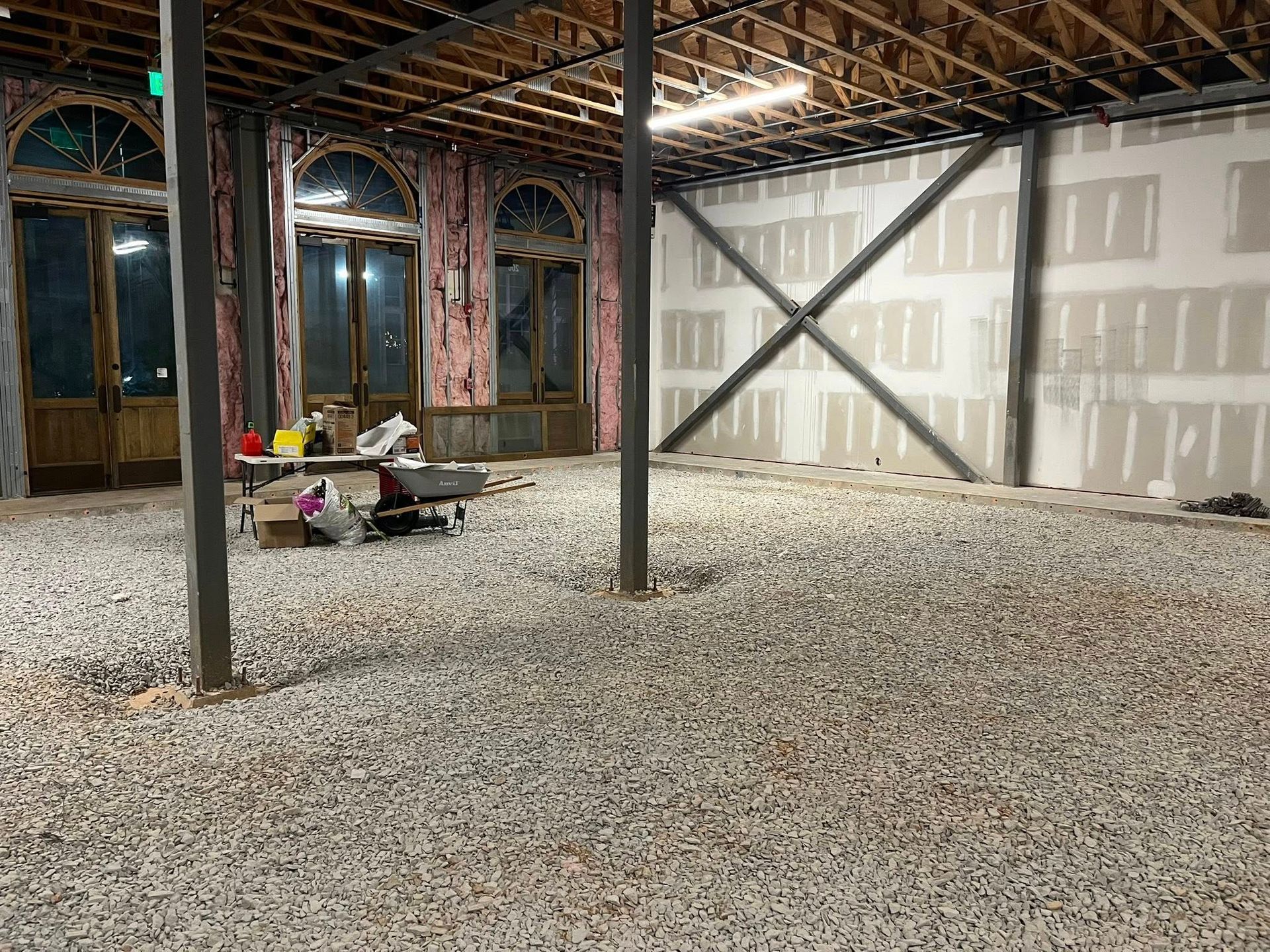 Interior of a building under construction featuring a gravel floor, exposed ceiling joists, and large arched windows.