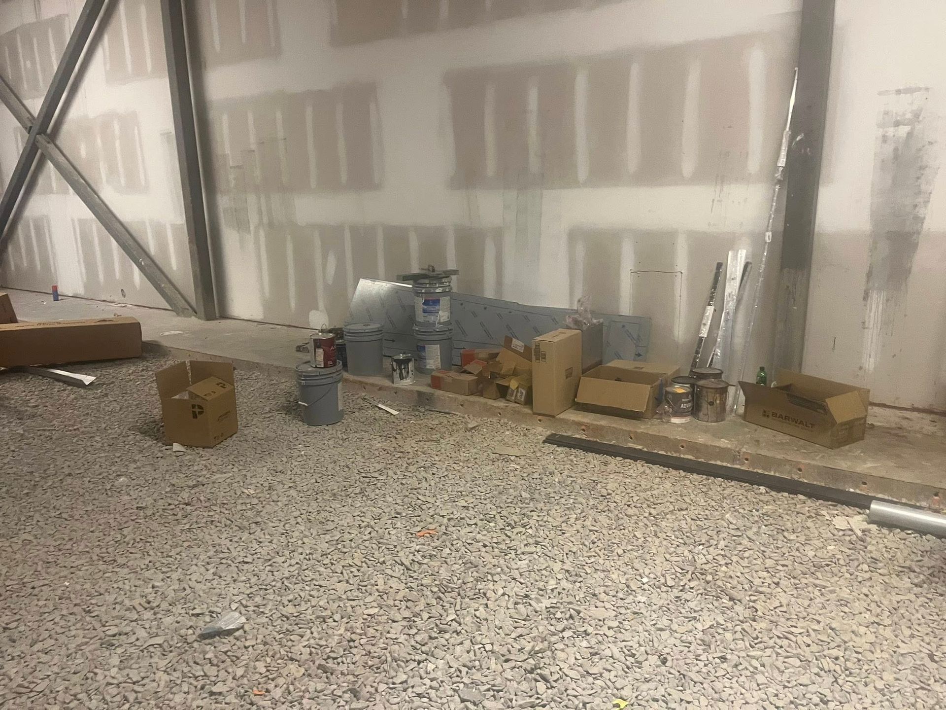 Construction materials and boxes stored along a wall with exposed steel structural supports and unfinished drywall.