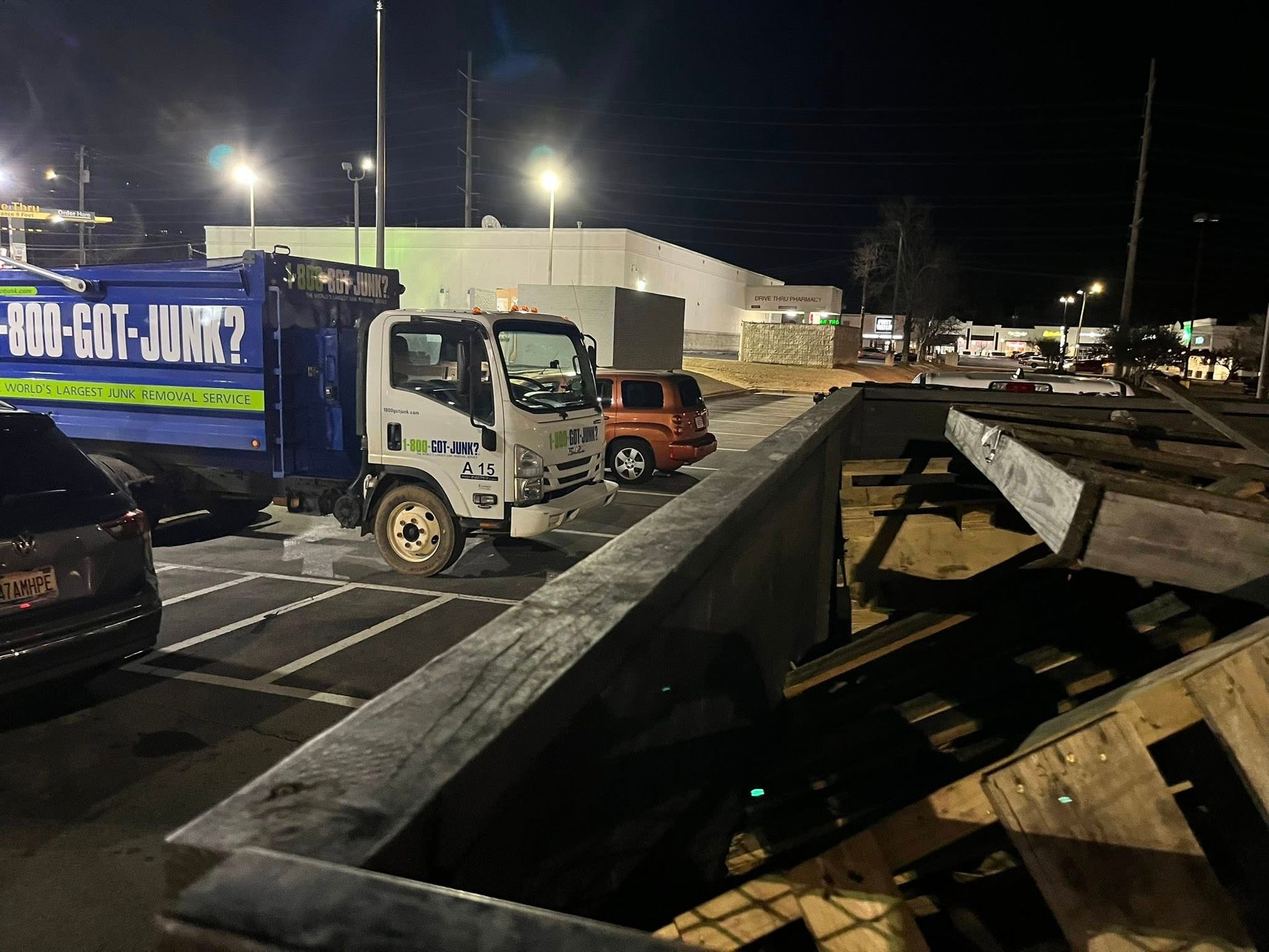 A 1-800-GOT-JUNK truck parked in a dark parking lot at night next to a large pile of wooden pallets.