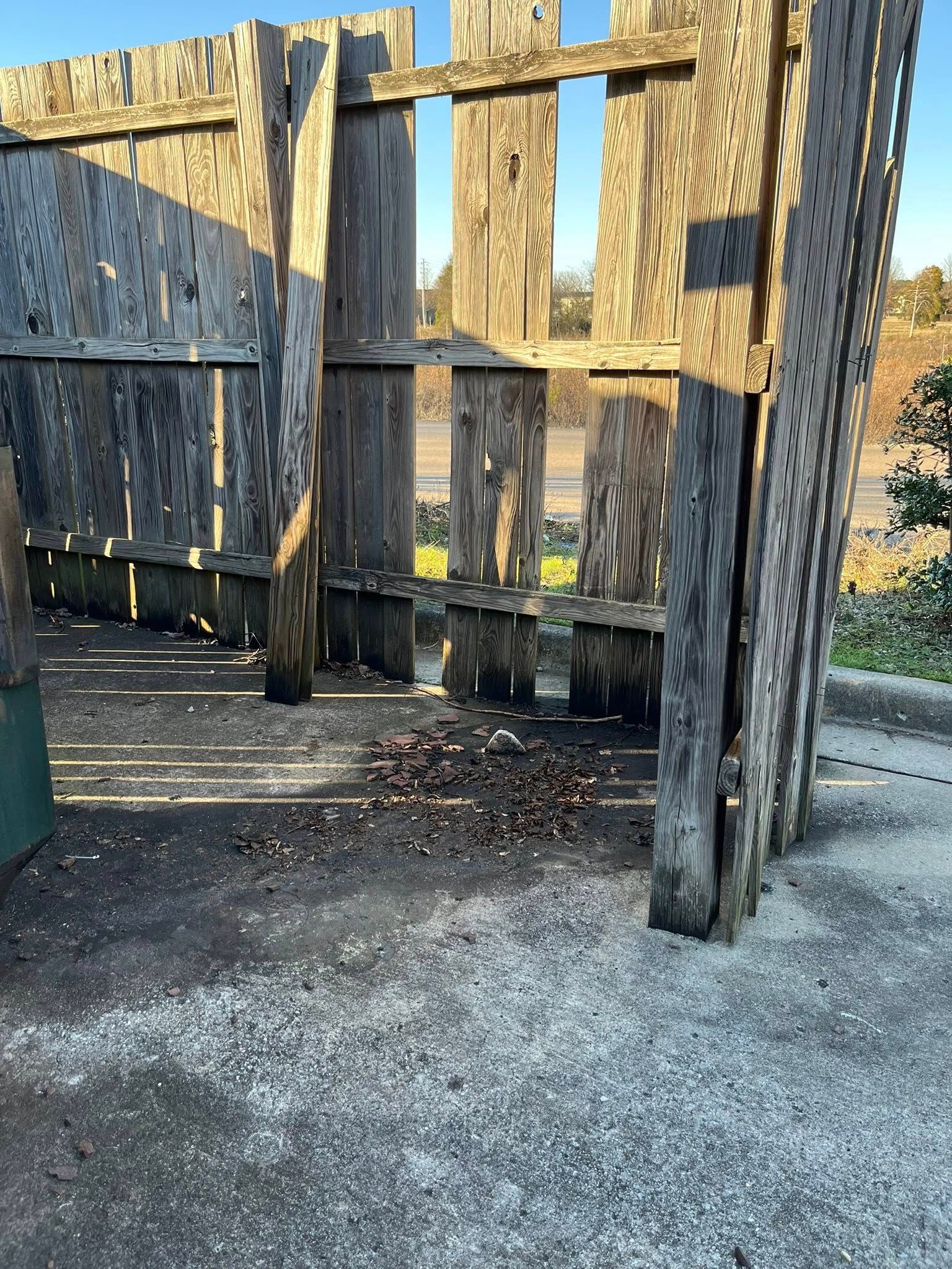 A wooden privacy fence enclosure containing debris on a concrete surface, with sunlight filtering through the slats.