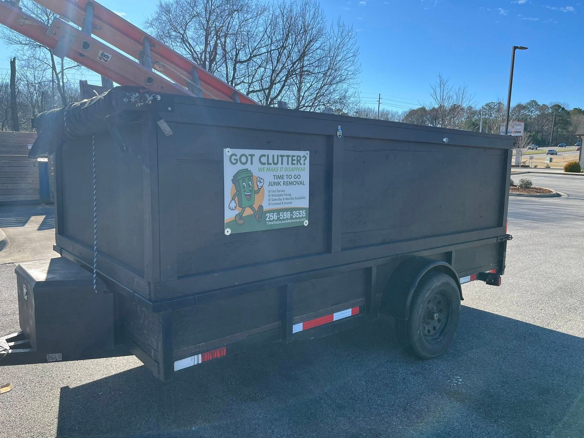 A black dump trailer parked on gravel, featuring a 