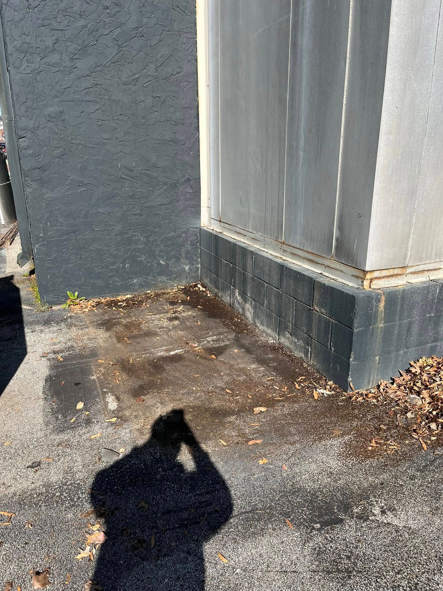 The corner of a building exterior where a dark gray textured wall meets a silver metal wall above a dark masonry base.