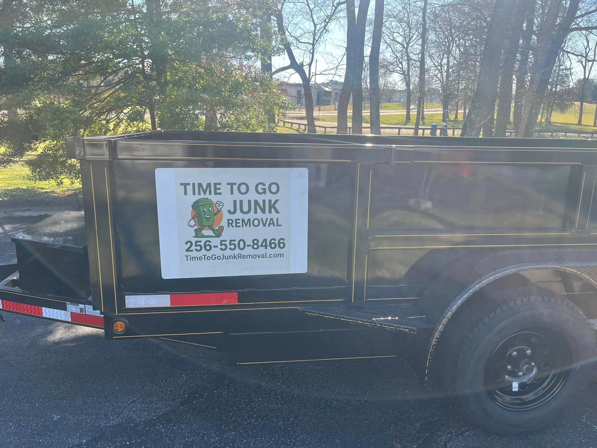 A black junk removal trailer parked outdoors with a sign featuring the business name and phone number.