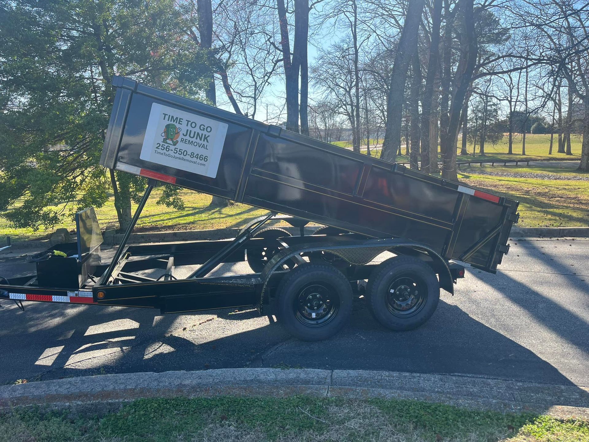 A black dump trailer parked outdoors on an asphalt surface with its bed raised in an angled, elevated position.