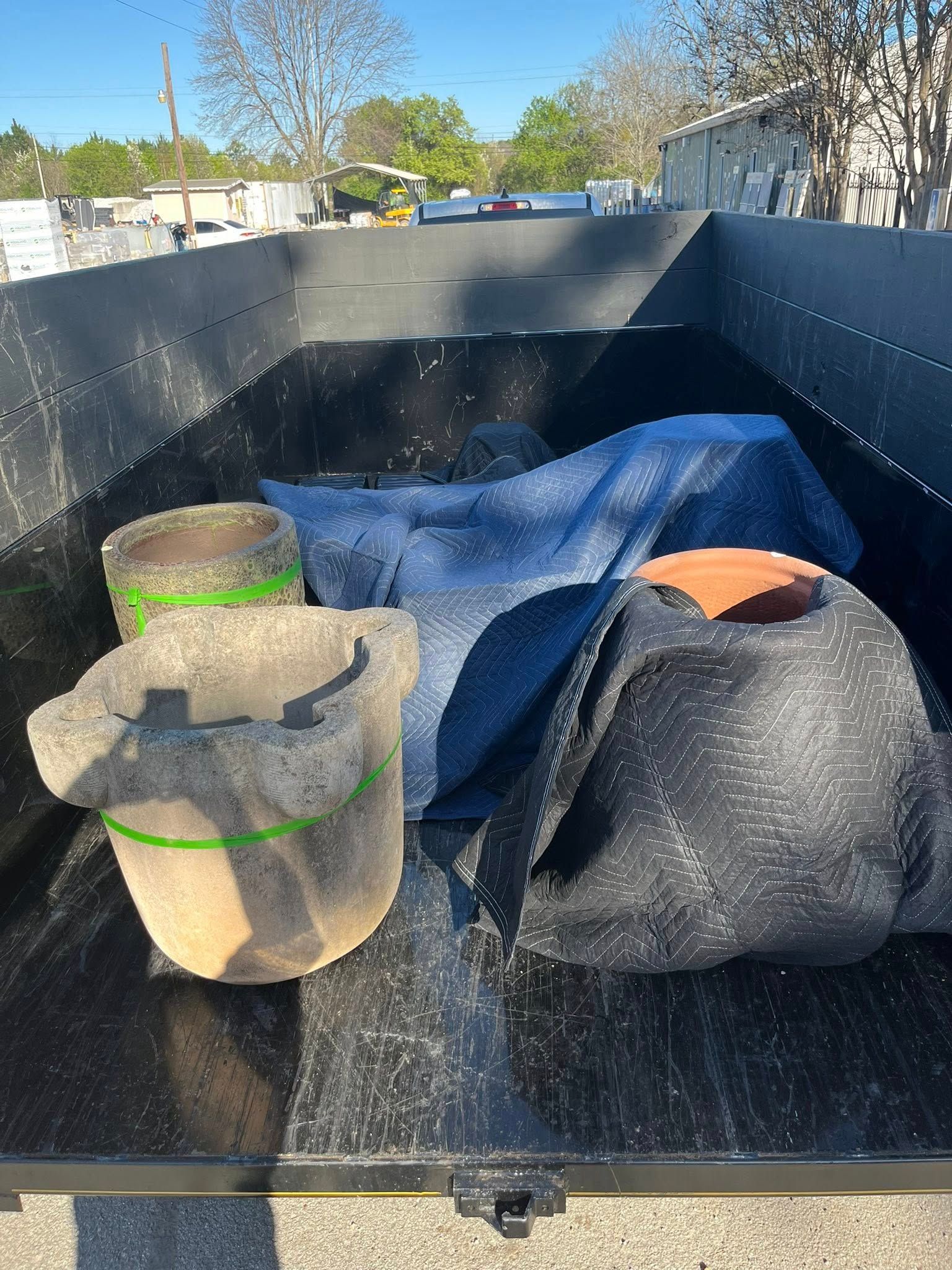 Three large, weathered terracotta-style pots sitting in the dark bed of an open utility trailer.