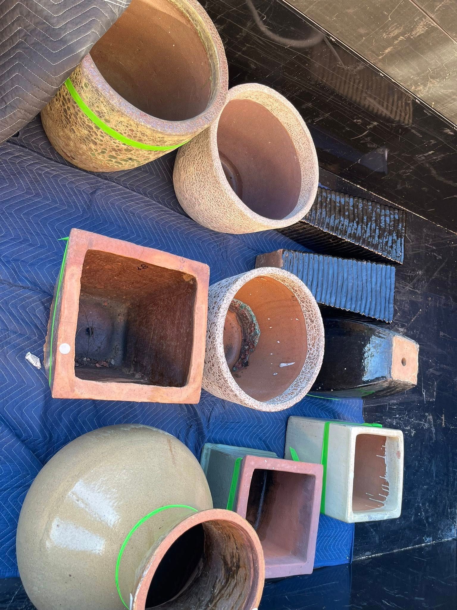 Various ceramic plant pots in different shapes, sizes, and colors arranged on a blue moving blanket.