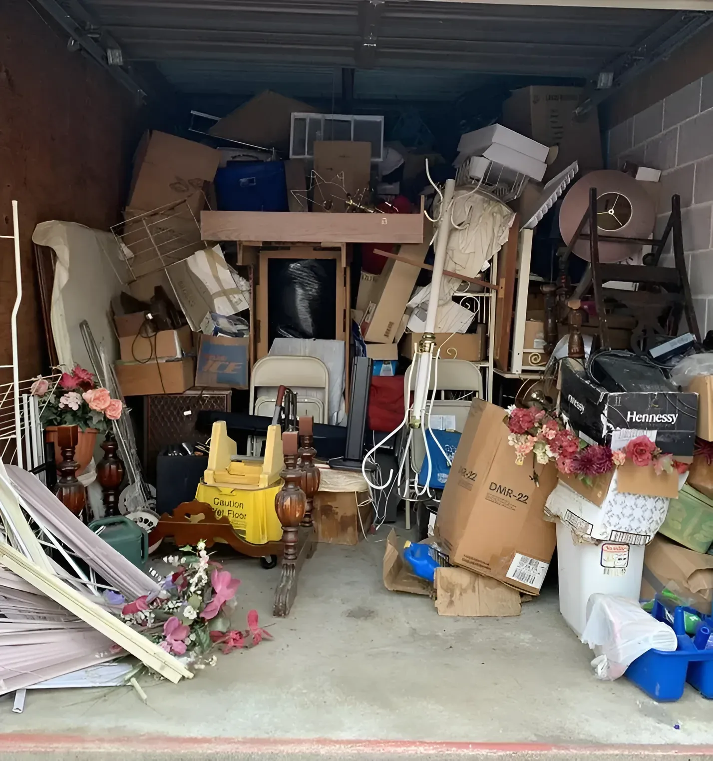 A cluttered storage unit filled with various boxes, furniture, decor items, and miscellaneous household goods.