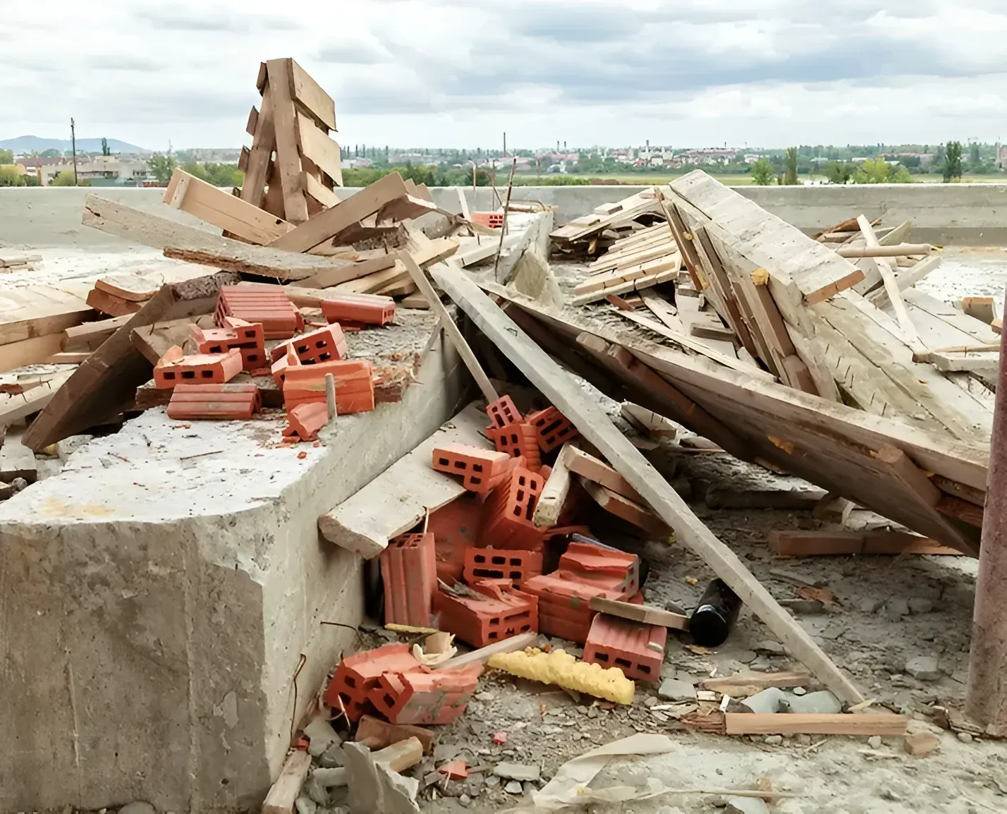 A pile of construction debris, including red hollow bricks, wooden beams, and concrete, at a building site.