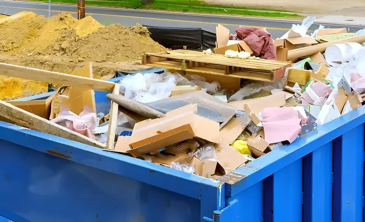 A large blue construction dumpster filled with wood scraps, cardboard, and construction debris.