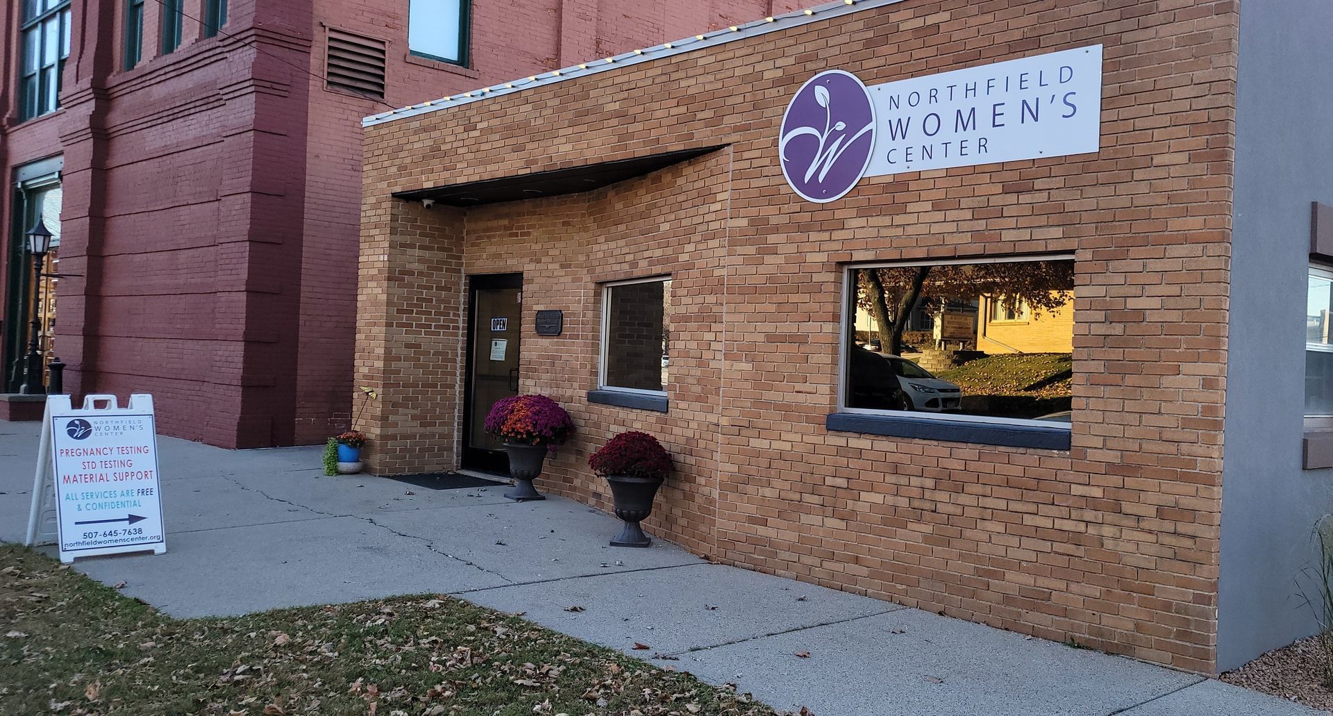 Building entrance with sign "Northfield Women's Center". Brick exterior, potted plants, sign.
