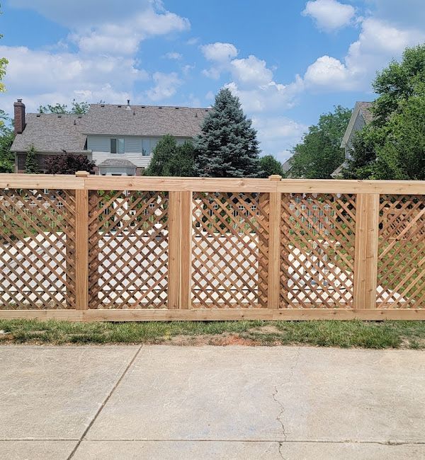 A wooden lattice fence surrounds a driveway in front of a house.