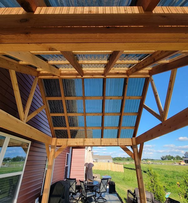 A wooden pergola with a clear roof and a table and chairs underneath it.