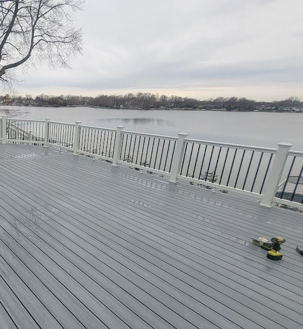 A gray deck with a white railing overlooking a lake.