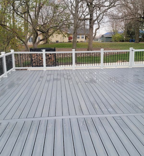 A gray deck with a white railing and trees in the background