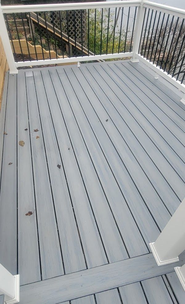 A gray deck with a white railing and a view of the water.