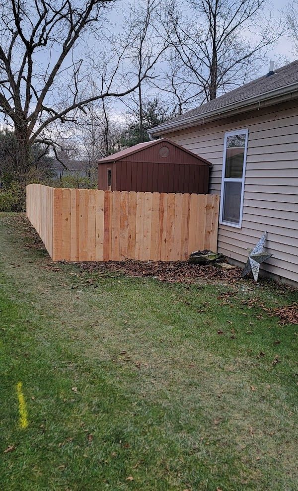 A wooden fence is in the backyard of a house next to a shed.