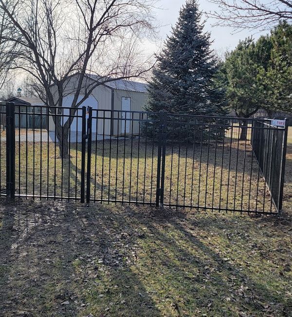 A metal fence surrounds a grassy yard with a garage in the background