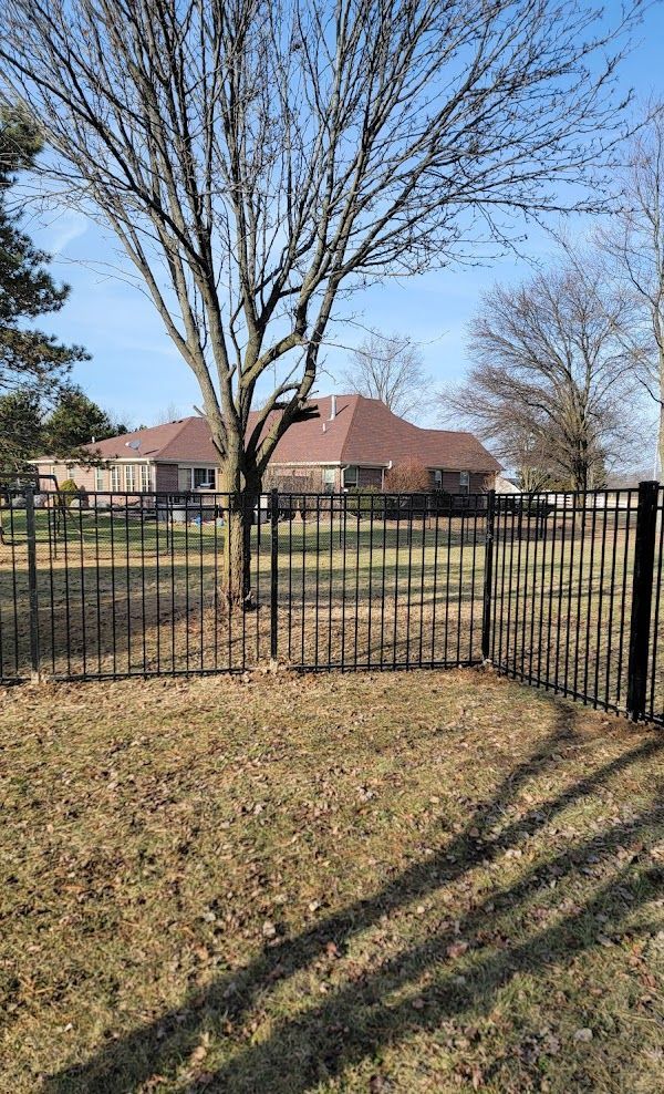 A black fence surrounds a grassy field with a house in the background.