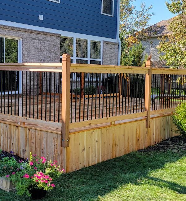A wooden fence surrounds a deck in front of a house.